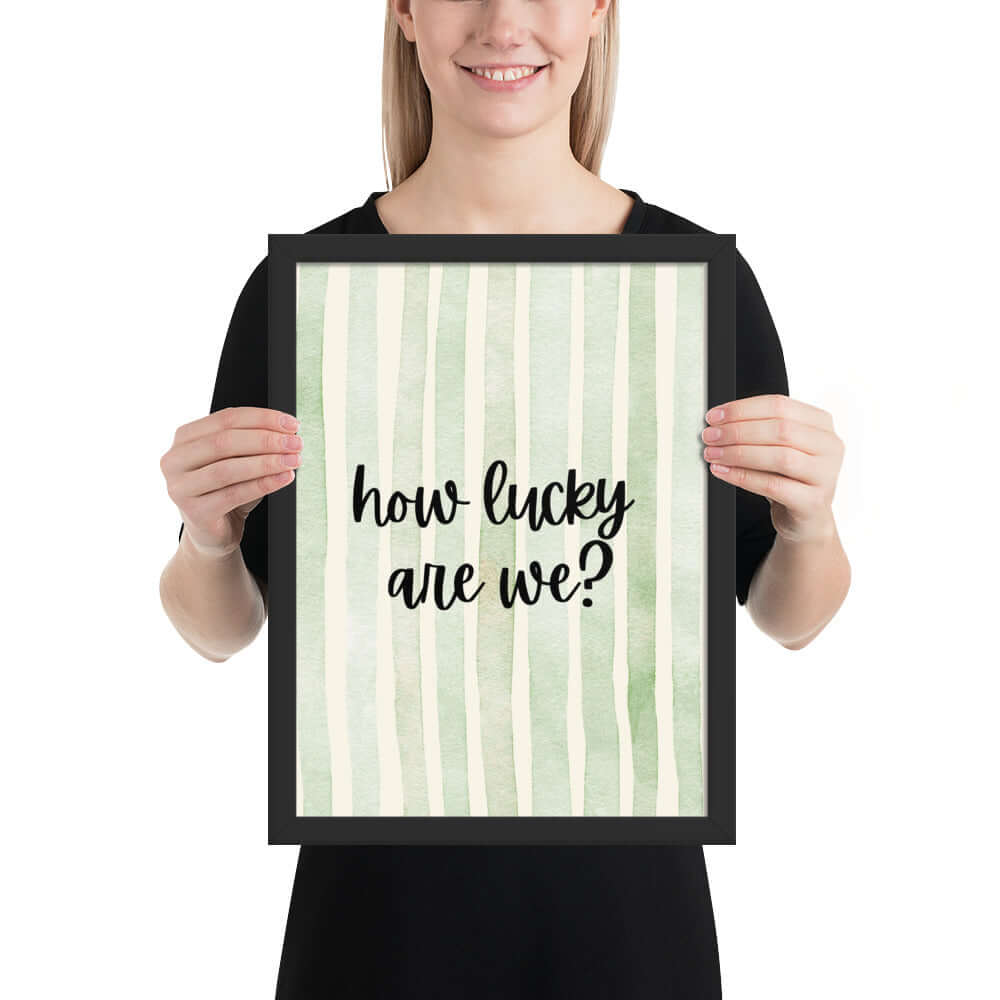 Person holding framed wall art with the phrase 'how lucky are we?' on a light green background.