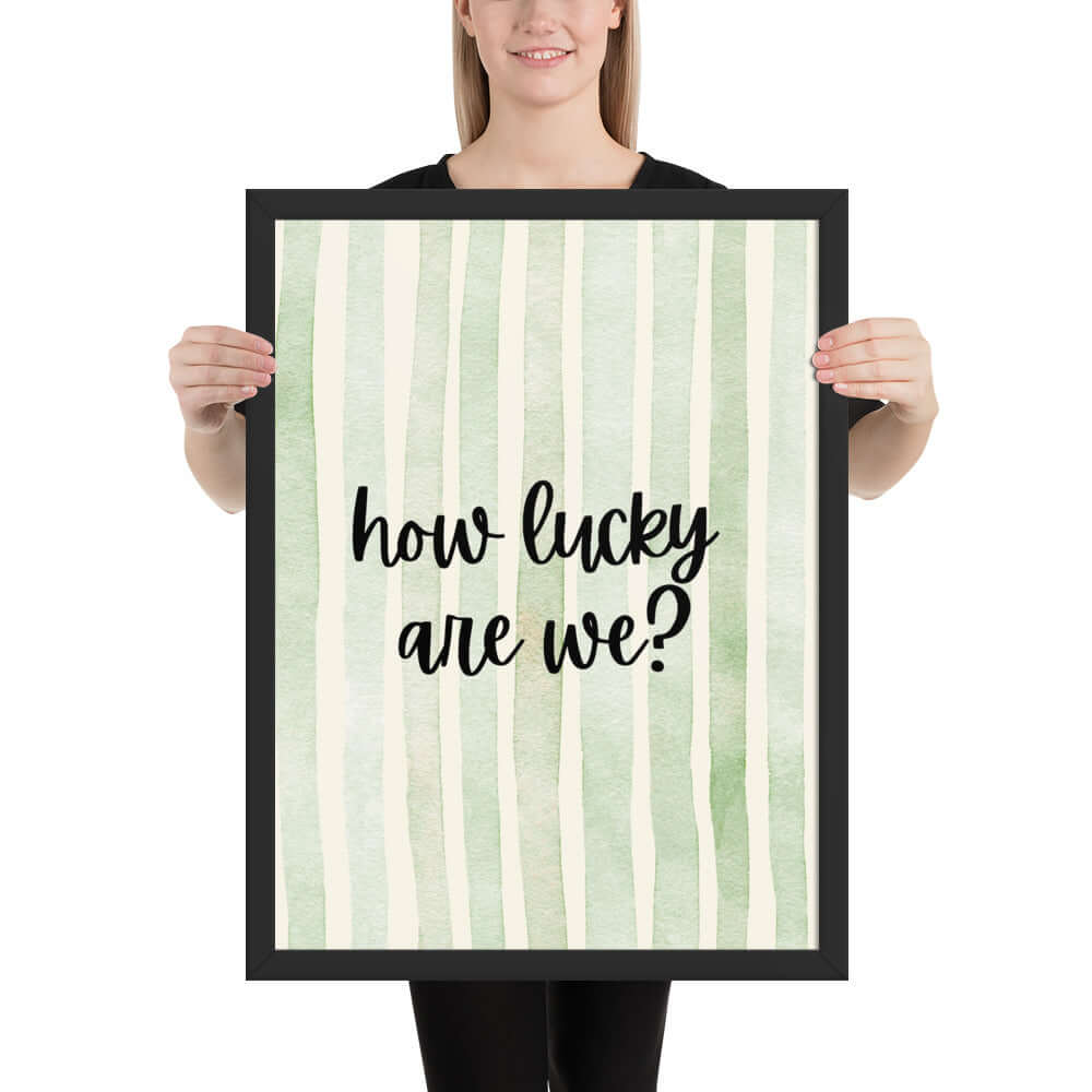 Framed wall art featuring the phrase 'how lucky are we?' displayed by a person with a green striped background.